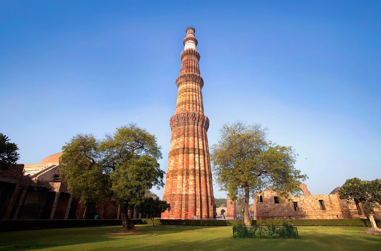 The tall brick minaret of Qutub Minar surrounded by ancient stone ruins in Delhi