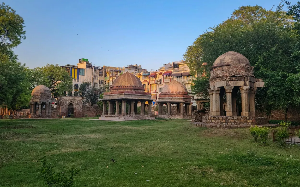 Historic stone pavilions and domes of Hauz Khas Fort with village buildings in the background