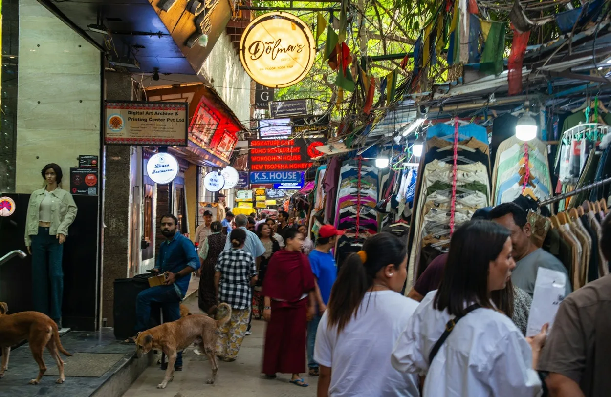 Narrow vibrant street lane in Majnu Ka Tilla featuring cafes, shops, and Tibetan flags
