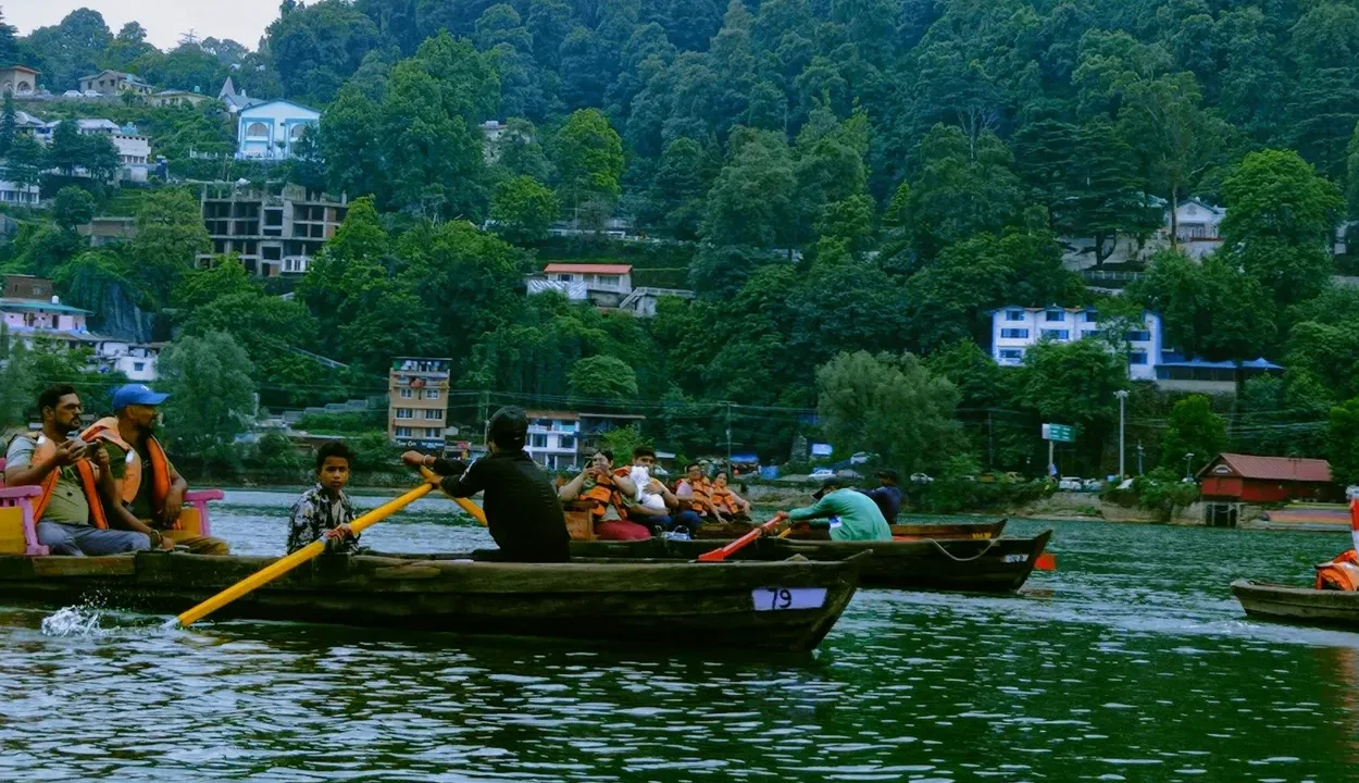 Tourists wearing orange life jackets enjoying a traditional rowboat ride on Naini Lake in Nainital.