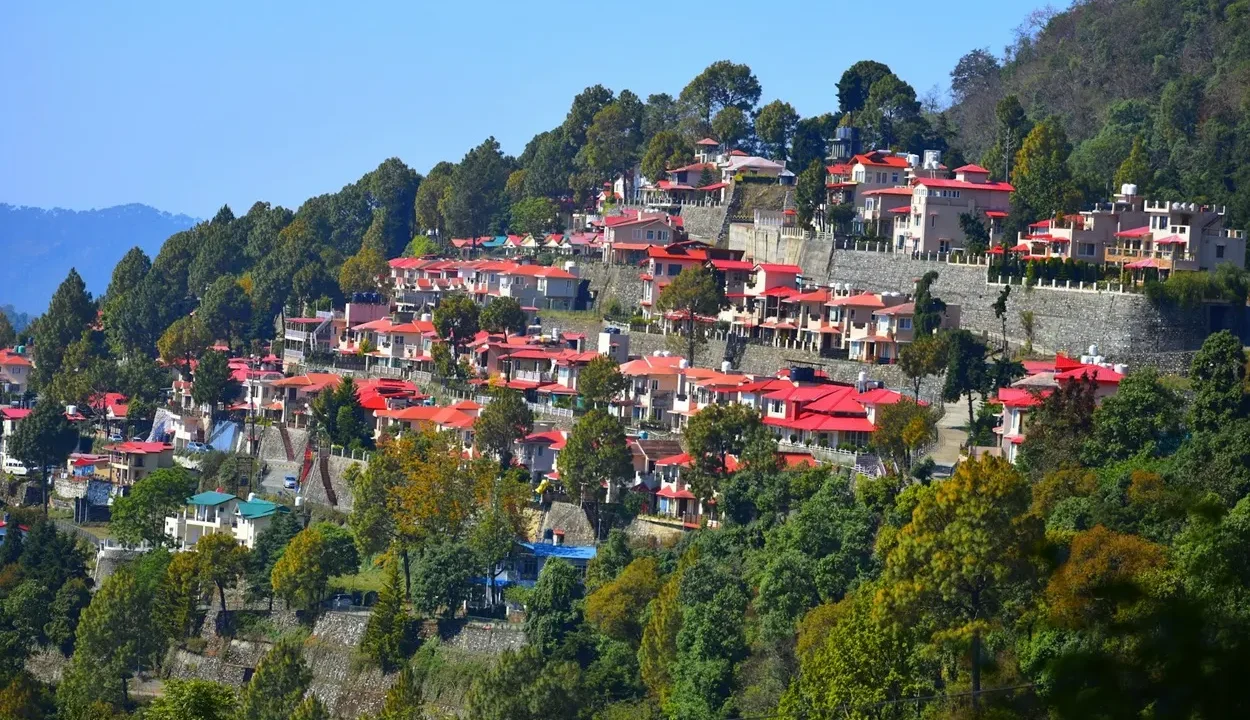Panoramic hillside view of red-roofed cottages and pine trees showcasing places where to stay in Nainital.