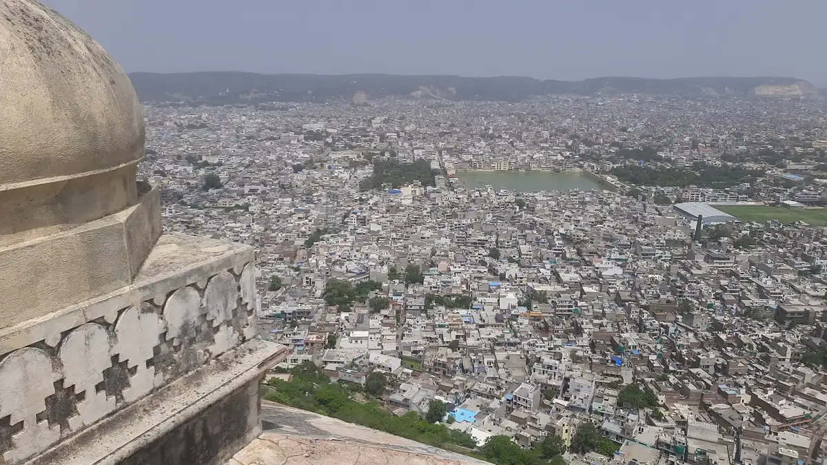 Aerial view of Jaipur city skyline and Aravalli hills framed by traditional stone dome architecture at Nahargarh Fort
