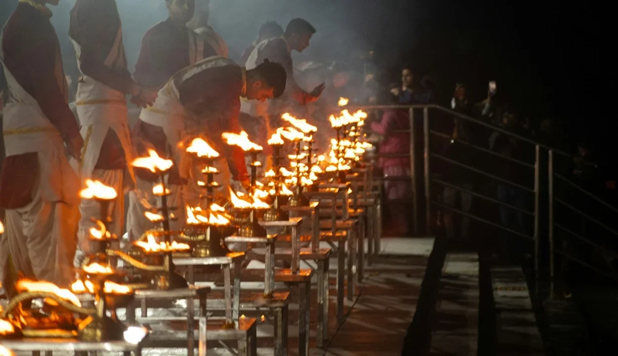 Priests holding multi-tiered brass oil lamps during the evening Ganga Aarti along the stepped stone terraces of Triveni Ghat in Rishikesh